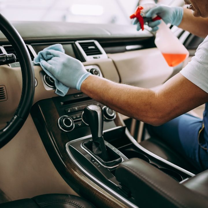 Person reinigt das Armaturenbrett eines Autos mit einem Mikrofasertuch und Spray.